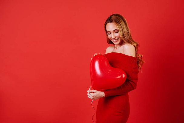 Young charming girl with long curly hair, in red dress holding air balloons, posing at camera. - Valokuva, kuva