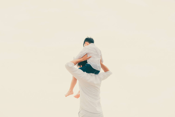 Feliz padre llevando a su hijo en el cuello en una playa de arena tropical en verano
. - Foto, imagen