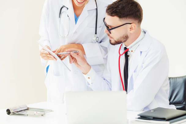 別の医師が患者の健康についての議論を持っていることとテーブルの上のノート パソコンに取り組んで病院事務所で医師. - 写真・画像