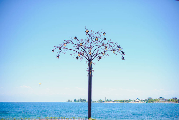 Μεταλλική κατασκευή. Δέντρο από μέταλλο για το φόντο της θάλασσας. Μπλε του ουρανού. Το νερό επιφάνειας κλαδιά δέντρων. Στο πλαίσιο του δέντρου. - Φωτογραφία, εικόνα