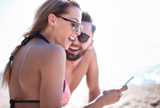 Smiling couple browsing their photos on the beach - Foto, Bild