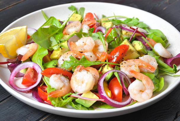 Avocado salad with shrimps, cherry tomatoes, arugula beet leaves, red onion, yellow sweet pepper. Healthy lunch plate with vegetables and shrimps  - Foto, Imagen