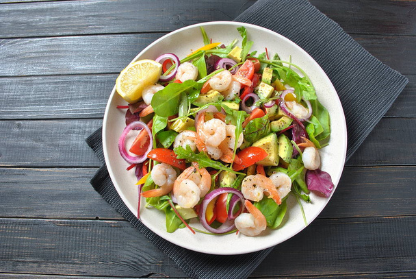 Avocado salad with shrimps, cherry tomatoes, arugula beet leaves, red onion, yellow sweet pepper. Healthy lunch plate with vegetables and shrimps  - Zdjęcie, obraz