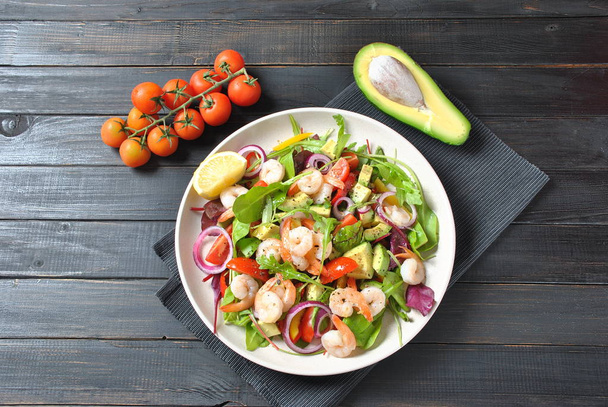 Avocado salad with shrimps, cherry tomatoes, arugula beet leaves, red onion, yellow sweet pepper. Healthy lunch plate with vegetables and shrimps  - Photo, image