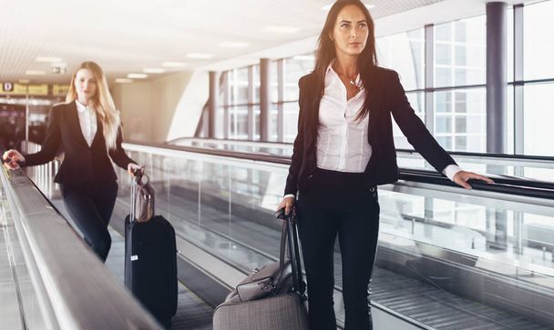 Twee ervan overtuigd vrouwen dragen formele pakken permanent op bewegende wandelpad in luchthaven - Foto, afbeelding