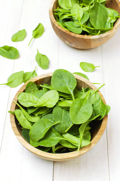 Fresh green spinach leaves on wooden bowl on white wooden rustic background top view copy space. Baby young spinach leaves, Ingredient for salad, healthy food, diet. Nutrition concept - Photo, Image