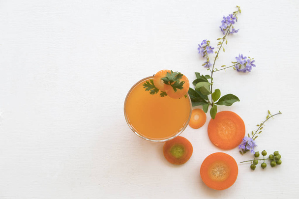 kasviperäisiä terveellisiä juomia porkkana ja sitruuna cocktail vettä sitruunaviipale, violetti kukkia koristelu tasainen antaa tyyli taustalla valkoinen puinen
 - Valokuva, kuva