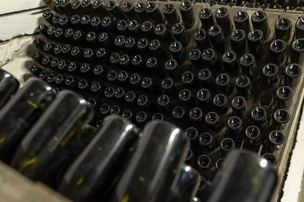 Винтажные бутылки с игристым вином на деревянных подставках в винодельне
 - Фото, изображение