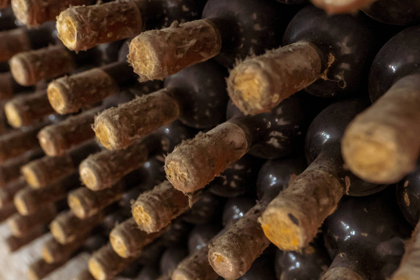 Крупный план стойки со старыми винными бутылками, покрытыми пылью и паутиной в винном погребе во Франции
 - Фото, изображение