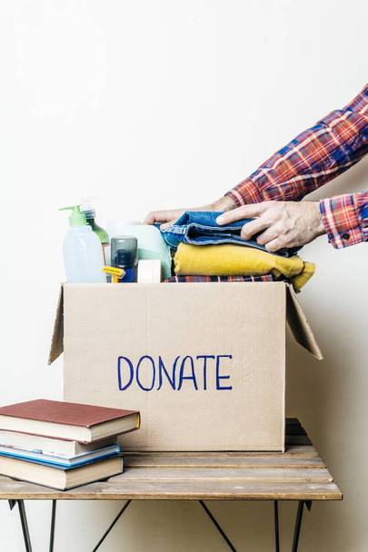 DONACIÓN DE ROPA Y CONCEPTO DE DONACIÓN ALIMENTARIA. Un hombre sosteniendo una caja de donaciones con ropa, zapatos y productos de higiene
. - Foto, Imagen