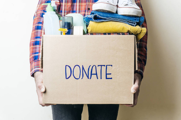 DONACIÓN DE ROPA Y CONCEPTO DE DONACIÓN ALIMENTARIA. Un hombre sosteniendo una caja de donaciones con ropa, zapatos y productos de higiene
. - Foto, Imagen