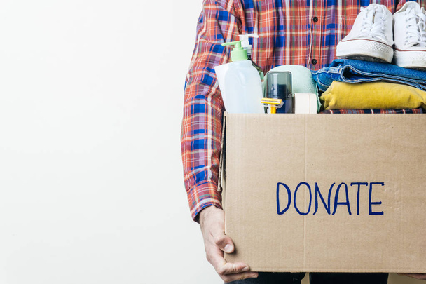 VÊTEMENTS DON ET DON ALIMENTAIRE CONCEPT. Un homme tenant une boîte de dons avec des vêtements, des chaussures et des produits d'hygiène. Espace de copie
 - Photo, image