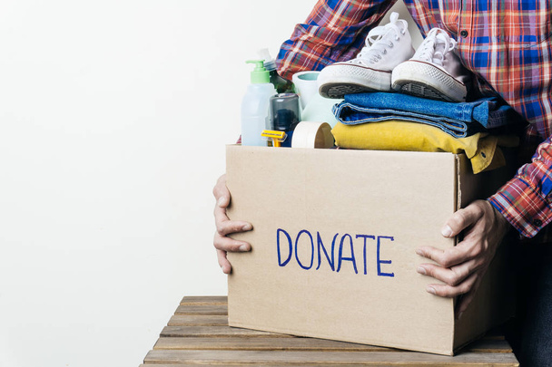 CLOTHES DONATION AND FOOD DONATION CONCEPT. A man holding a donation box with clothes, shoes and hygiene products. Copy space - Photo, image