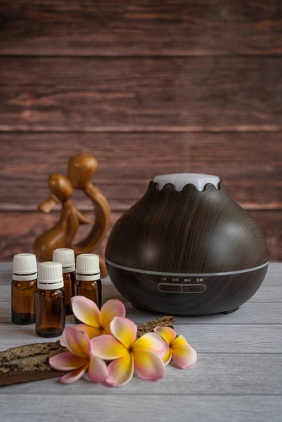 Difusor de óleo essencial com flores frescas de frangipani, garrafas de óleo de vidro, alguma madeira crua e uma estátua de amor de madeira
 - Foto, Imagem