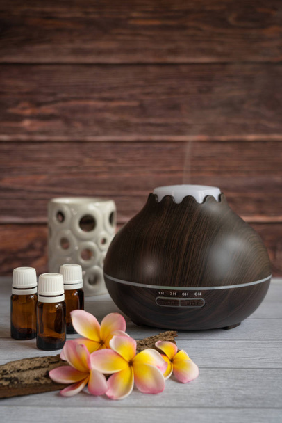 Difusor de óleo essencial com flores frescas de frangipani, garrafas de óleo de vidro, alguma madeira crua e uma vela de luz de chá branco
 - Foto, Imagem