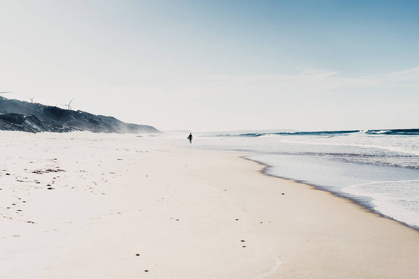 man surfer on the beach with surfboard, walks along the ocean shore, Nazar, Portugal. - Φωτογραφία, εικόνα
