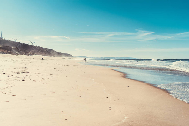 man surfer on the beach with surfboard, walks along the ocean shore, Nazar, Portugal. - Fotó, kép