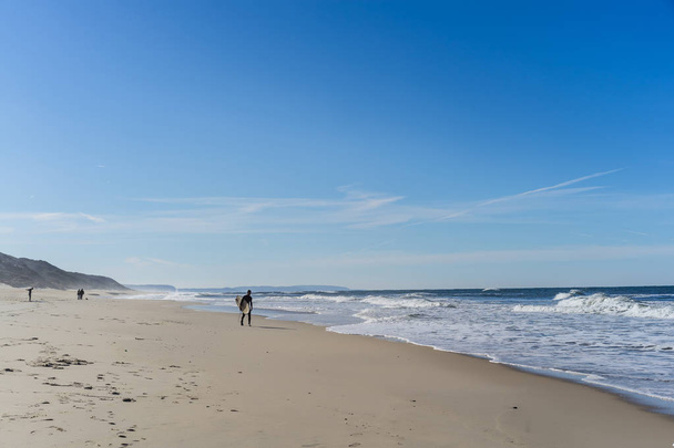 man surfer on the beach with surfboard, walks along the ocean shore, Nazar, Portugal. - Fotó, kép