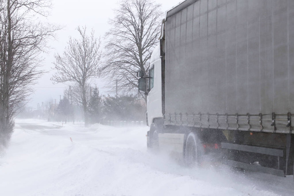 Большой грузовик пробирается через снежные заносы по опасной дороге, покрытой снегом. TIR воюет с зимним элементом. Трудности в движении во время метели. Последствия холодной погоды и воды
. - Фото, изображение