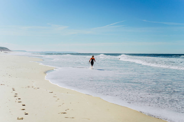 surf girl on the ocean coast in a wet suit with surf board, Nazar, Portugal. - Fotó, kép
