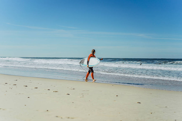 Nazar、ポルトガルのサーフボードとウェット スーツで海の海岸にサーフィン女の子. - 写真・画像