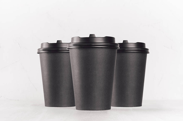 Coffee mockup - group of three blank black paper cups with cap closeup on white wood table, coffee shop interior. Modern elegant concept for branding identity, advertising, design. - Фото, зображення