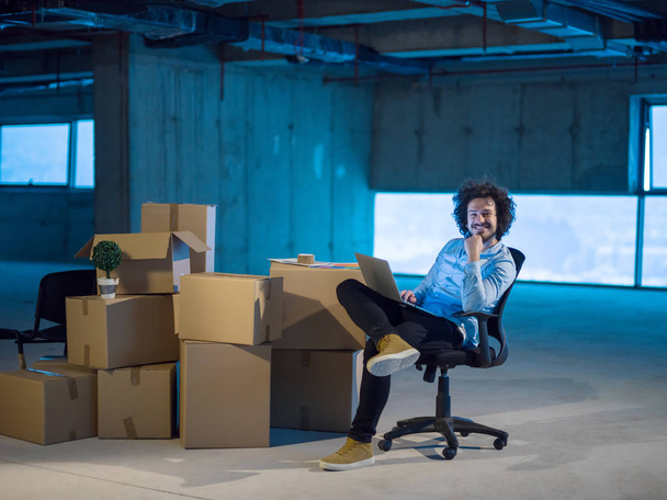 young male architect on construction site checking documents and business workflow using laptop computer with cardboard boxes around him in new startup office - Foto, Bild