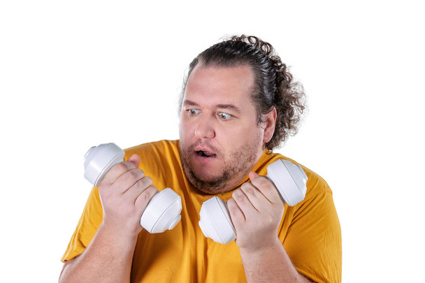 Funny fat man exercising with dumbbells and looking at camera isolated - Photo, image
