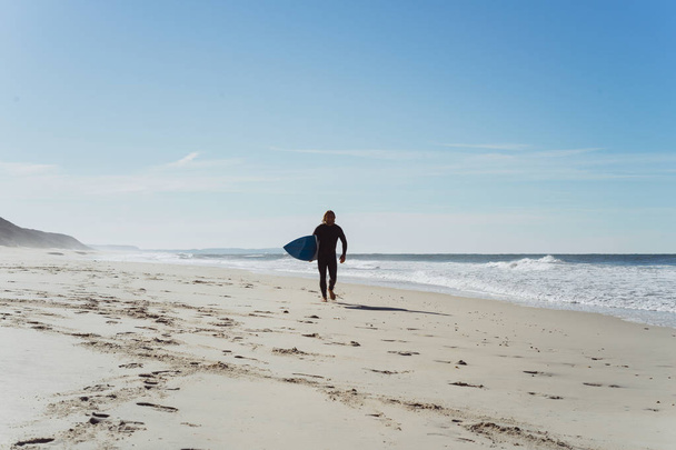Hombre con tabla de surf en la orilla del océano. Surfista con traje de neopreno. Nazare, Portugal
. - Foto, imagen