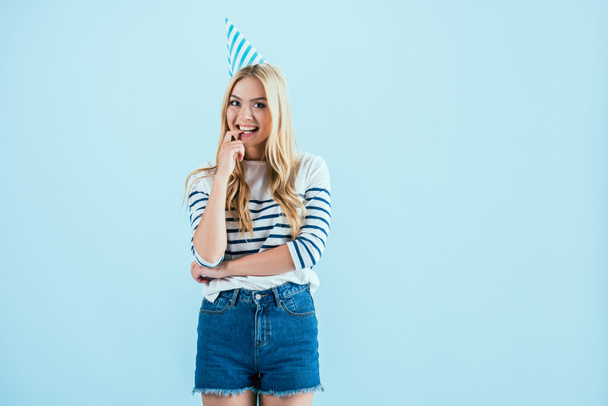 Girl in party hat biting finger isolated on blue - Photo, Image