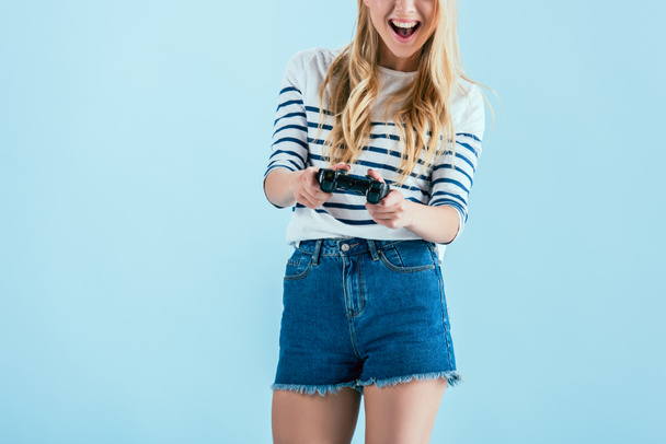 Weergave van lachen jonge vrouw bijgesneden met gamepad geïsoleerd op blauw - Foto, afbeelding