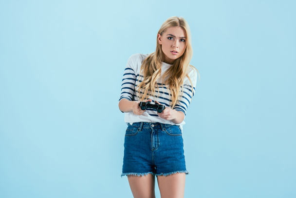 Hermosa chica rubia concentrada jugando videojuegos con joystick aislado en azul
 - Foto, Imagen