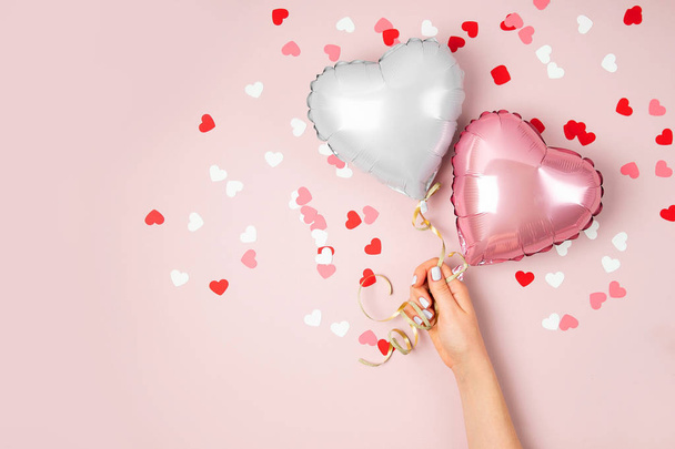 Female hands holding balloons of hearts shaped foil on pastel pink background - Foto, imagen