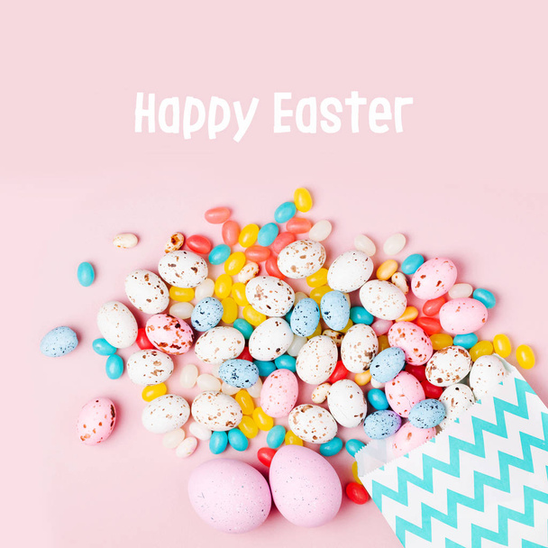 Easter candy chocolate eggs and Jellybean flowing from party paper bag  on pink background - Fotoğraf, Görsel