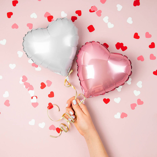 Female hands holding balloons of hearts shaped foil on pastel pink background - Valokuva, kuva