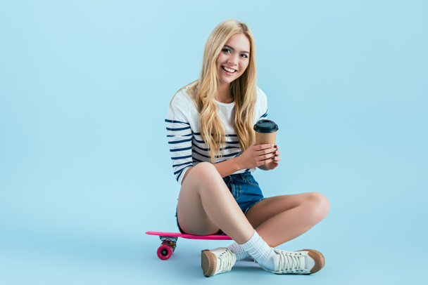 Beautiful girl sitting on longboard with cup of coffee on blue background - Foto, Imagem
