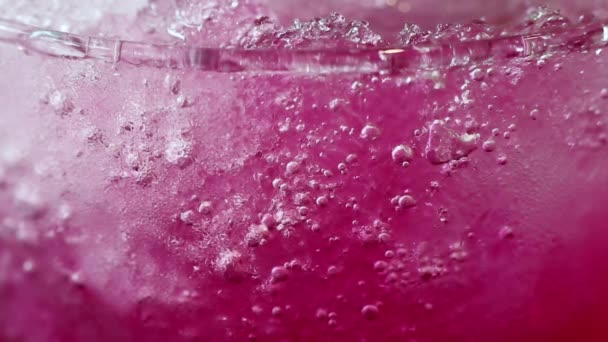 Abstracte schoonheid in drankje details. Extreme close-up iced rode frisdrank drinken in glas. Crushed ijs en koolzuurhoudende bubbels maken mooie textuur patronen. - Video