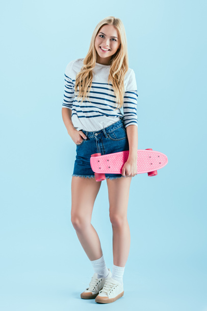Excited girl with longboard posing with hand in pocket on blue background - Foto, Imagem