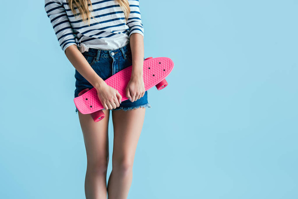 Partial view of young woman holding pink longboard on blue background - Fotoğraf, Görsel