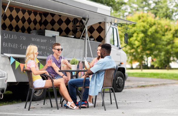 friends with drinks sitting at table at food truck - Photo, image