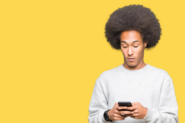 Young african american man with afro hair using a smartphone scared in shock with a surprise face, afraid and excited with fear expression - Photo, Image
