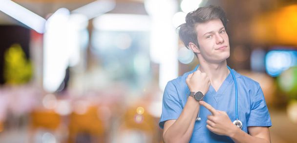Młody lekarz sobie uniform medyczny na białym tle w pośpiechu wskazującego oglądać czas, niecierpliwość, zdenerwowany i zły za opóźnienie terminu - Zdjęcie, obraz