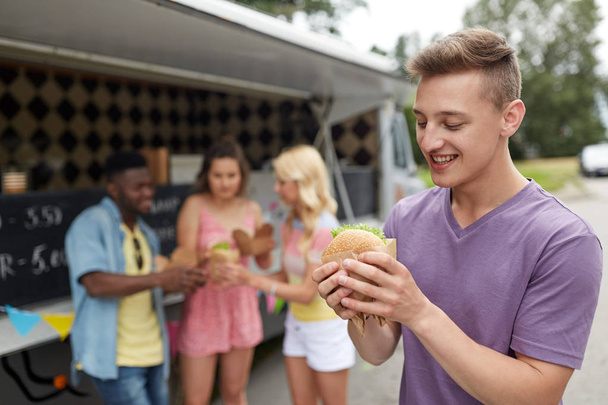 happy man with hamburger and friends at food truck - Foto, Imagen