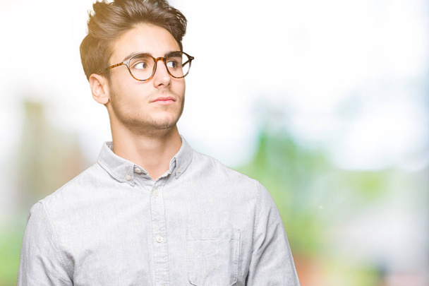Mladý pohledný muž nosí brýle izolované pozadí vypadající strana a vytřeštěné pryč myšlení. - Fotografie, Obrázek