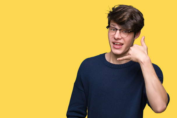 Young handsome man wearing glasses over isolated background smiling doing phone gesture with hand and fingers like talking on the telephone. Communicating concepts. - 写真・画像