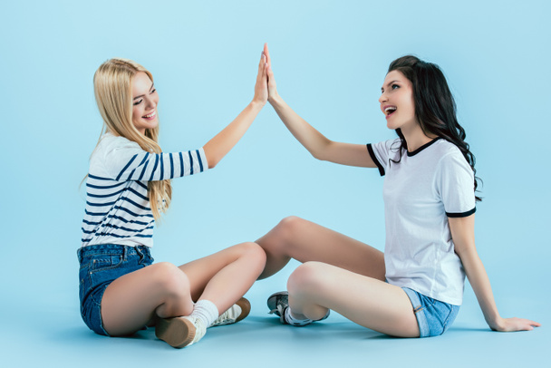 Iloinen tytöt denim shortsit poseeraa lattialla sinisellä pohjalla
 - Valokuva, kuva