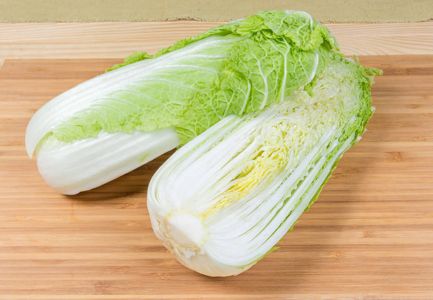Two halves of head napa cabbage  cut along, also known as chinese cabbage on the bamboo wooden cutting board - Photo, Image