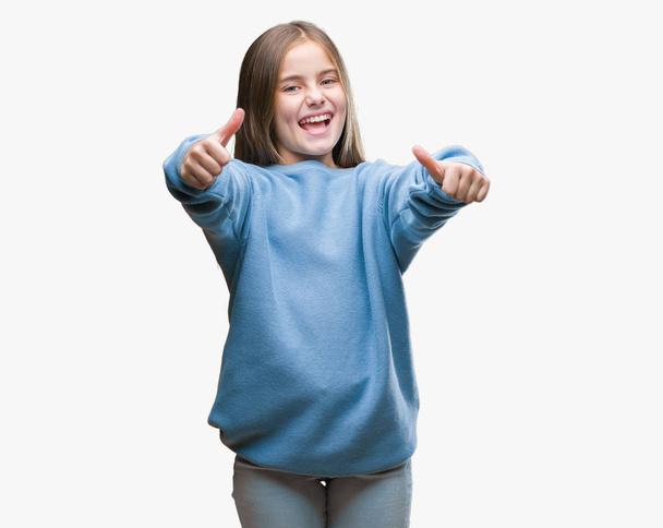 Young beautiful girl wearing winter sweater over isolated background approving doing positive gesture with hand, thumbs up smiling and happy for success. Looking at the camera, winner gesture. - Фото, зображення