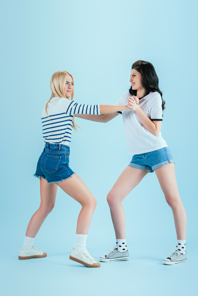Aggressive girls in denim shorts fighting on blue background - Фото, изображение