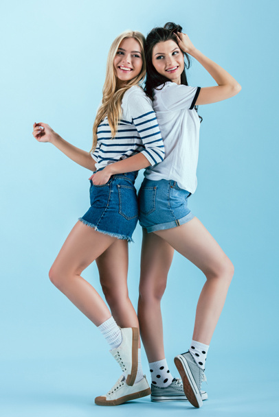 Excited girls posing back to back on blue background - 写真・画像
